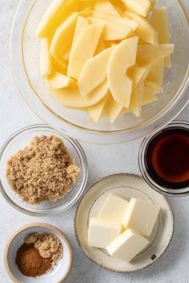 Clear glass mixing bowls filled with sliced apples, brown sugar, butter, pure maple syrup for fried apple recipe.