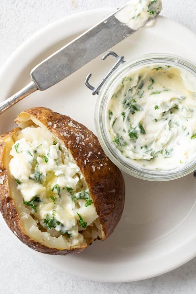 A white plate with a baked potato and glass jar filled with a creamy spread.
