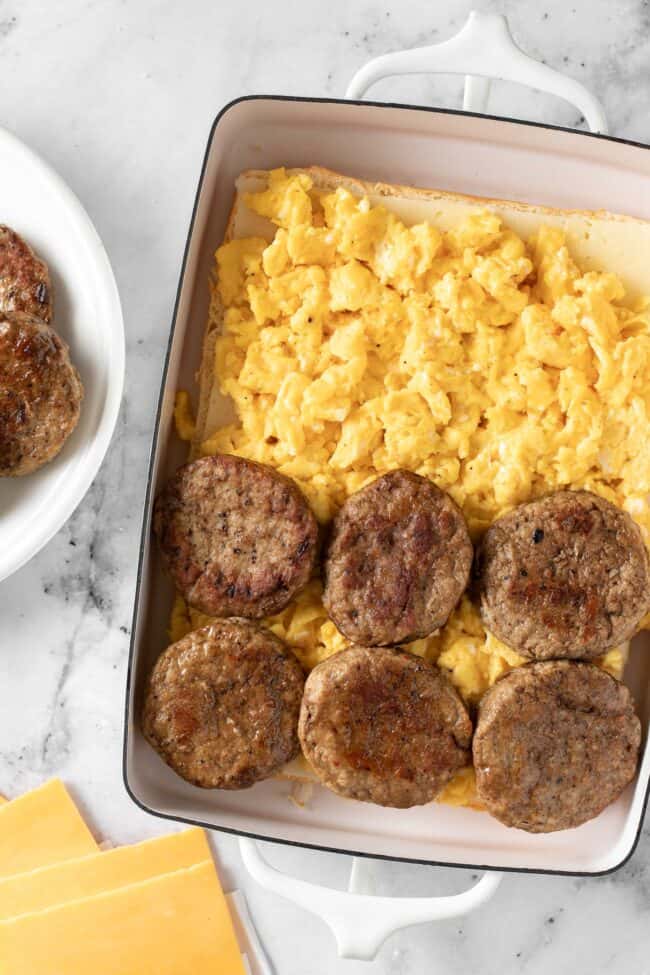 A white baking dish filled with scrambled eggs and sausage for breakfast sliders.