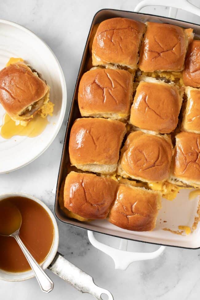 A white baking dish filled with breakfast sliders (rolls filled with scrambled eggs, sausage patties and cheese).
