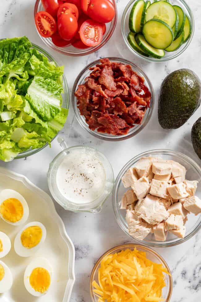 Clear glass bowls filled with chopped meat, lettuce, cucumber and tomatoes.