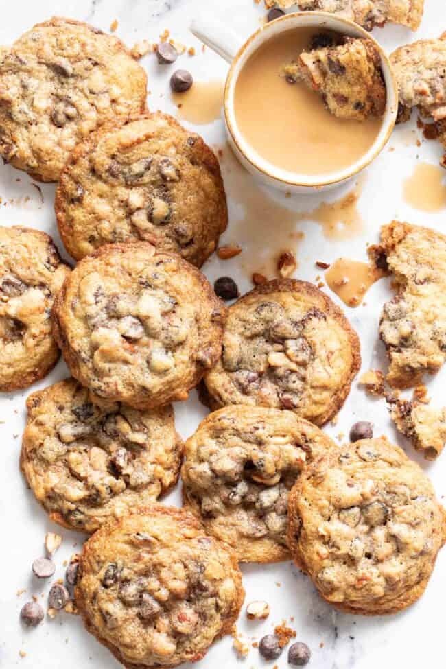 Several cowboy cookies set on a white counter with a cup of coffee next to them.