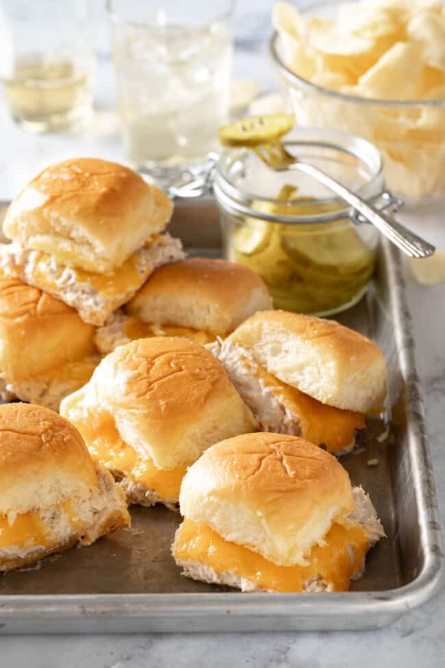 A cookie sheet filled with small sandwiches. A bowl of potato chips sits next to the cookie sheet.