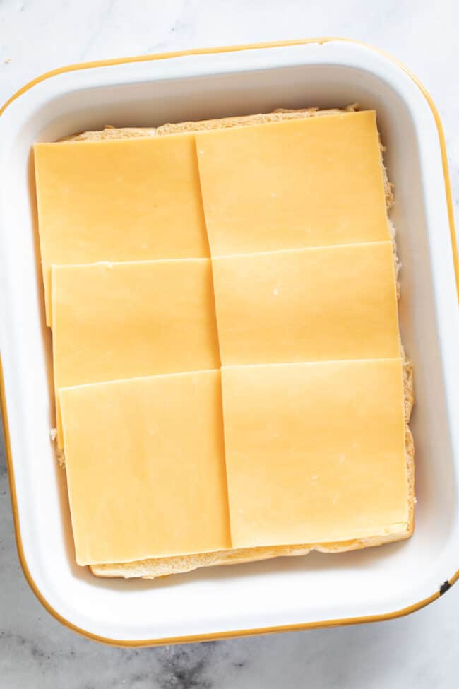 A white baking dish with slices of cheddar cheese on Hawaiian rolls.