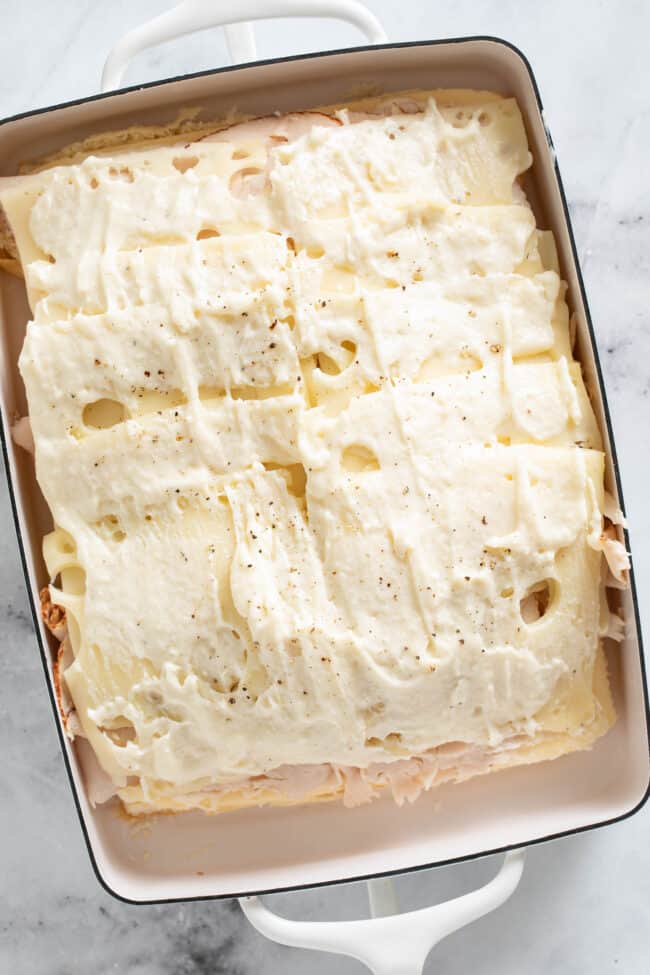 A white baking dish with Hawaiian rolls and lunch meat in it.