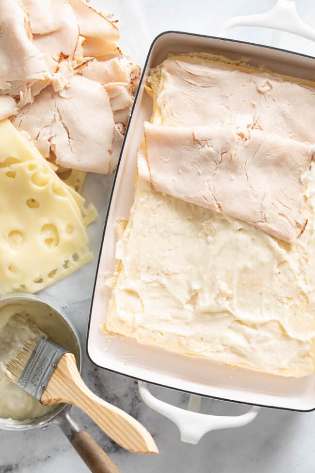 A white baking dish with bread and lunch meat in it.