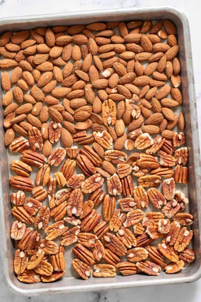 A cookie sheet with raw almonds and pecans on it.