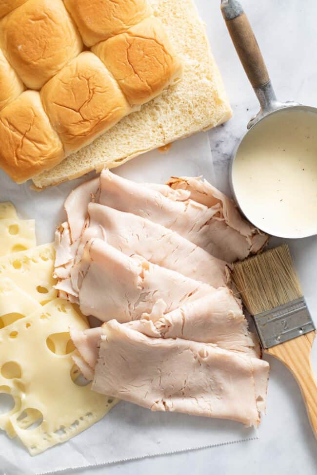 Hawaiian rolls on a counter top next to sliced turkey and cheese.