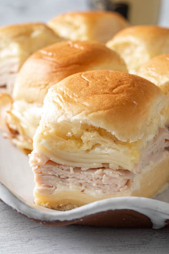 A platter filled with Hawaiian roll Turkey Sliders made with turkey slices, cheese and Bechamel sauce.