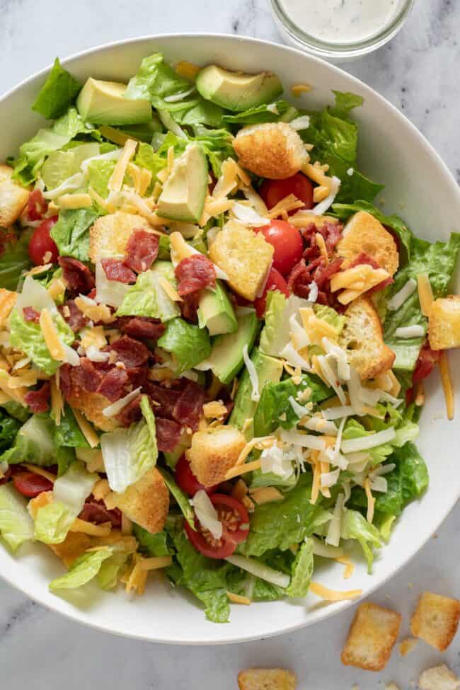 A white bowl filled with chopped lettuce, croutons, cherry tomatos and avocado.