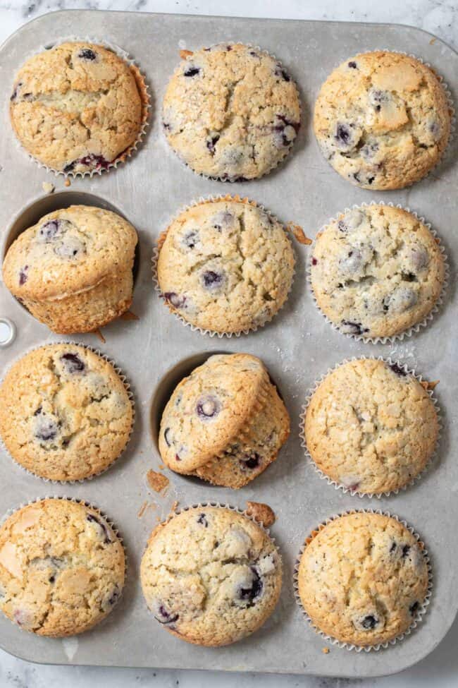 A muffin tin filled with baked blueberry muffins.