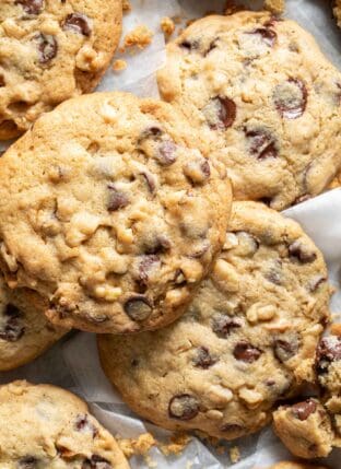 Several chocolate chip cookies scattered on bakers paper.