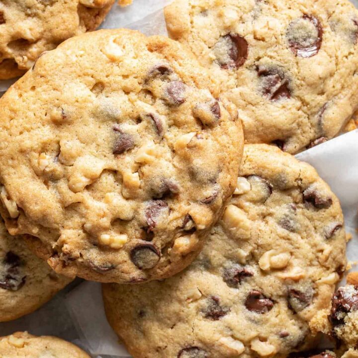 Several chocolate chip cookies scattered on bakers paper.