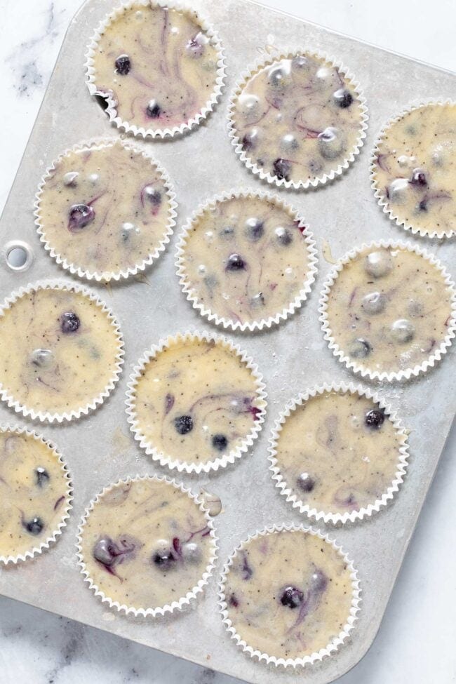 A aluminum muffin tin filled with batter for blueberry muffins.