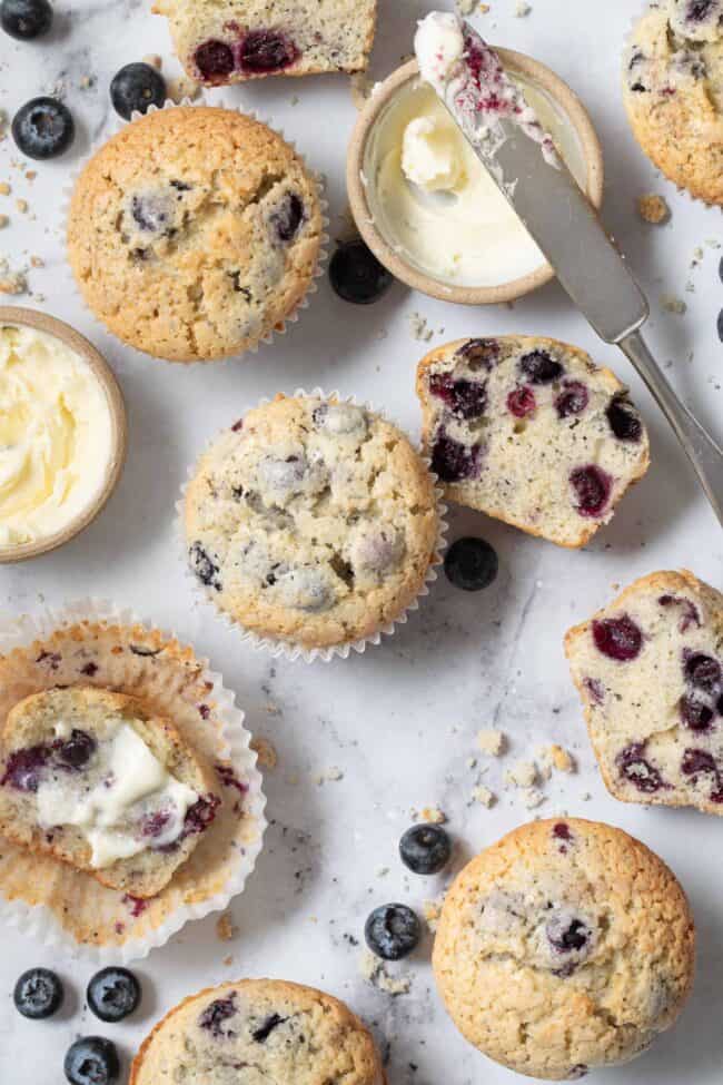 Several blueberry muffins scattered on a marble countertop.