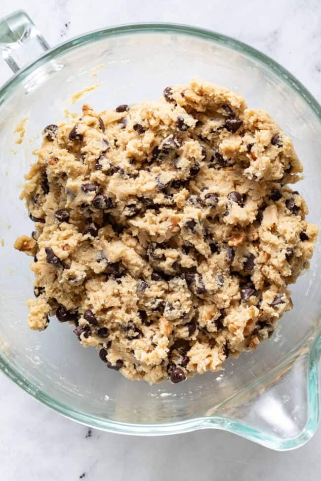 A clear glass mixing bowl filled with chocolate chip cookies dough