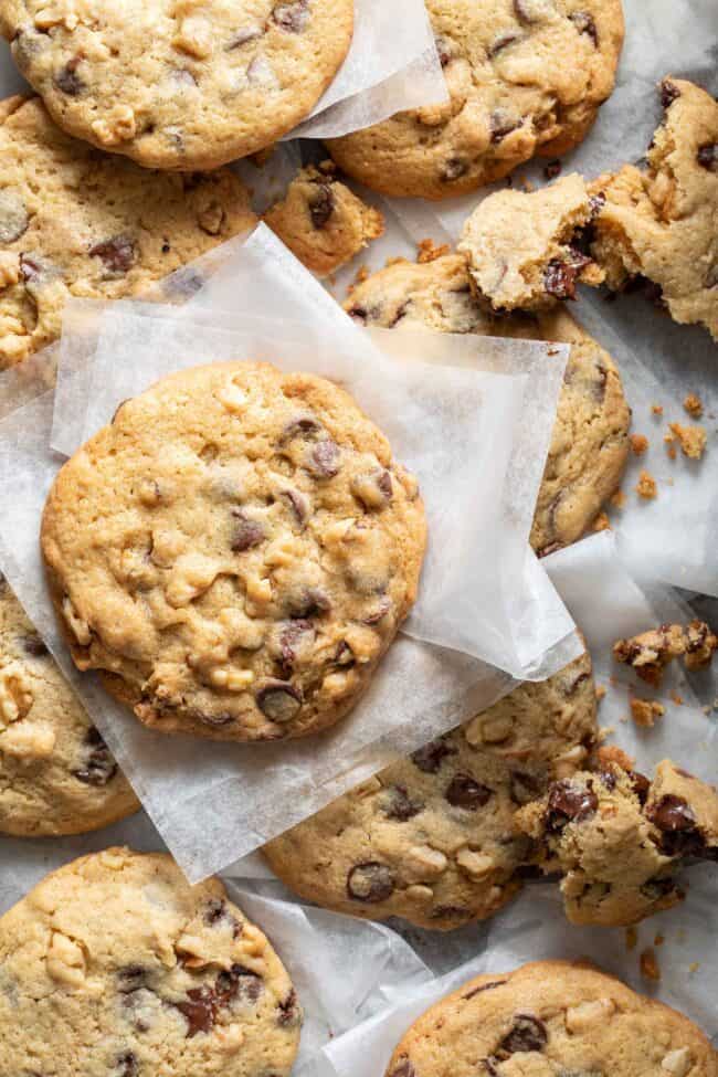 Several chocolate chip cookies scattered on bakers paper.