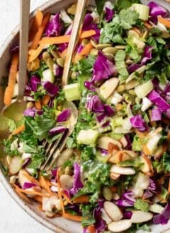 A tan bowl filled with Chopped Kale Salad (curly kale, cabbage, carrots, celery, fresh mint, golden raisins and almond slices.