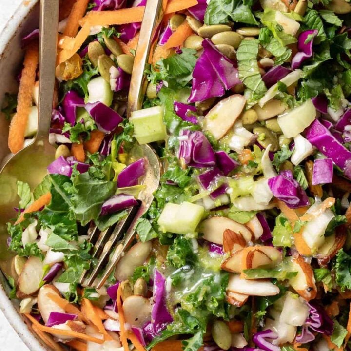 A tan bowl filled with Chopped Kale Salad (curly kale, cabbage, carrots, celery, fresh mint, golden raisins and almond slices.