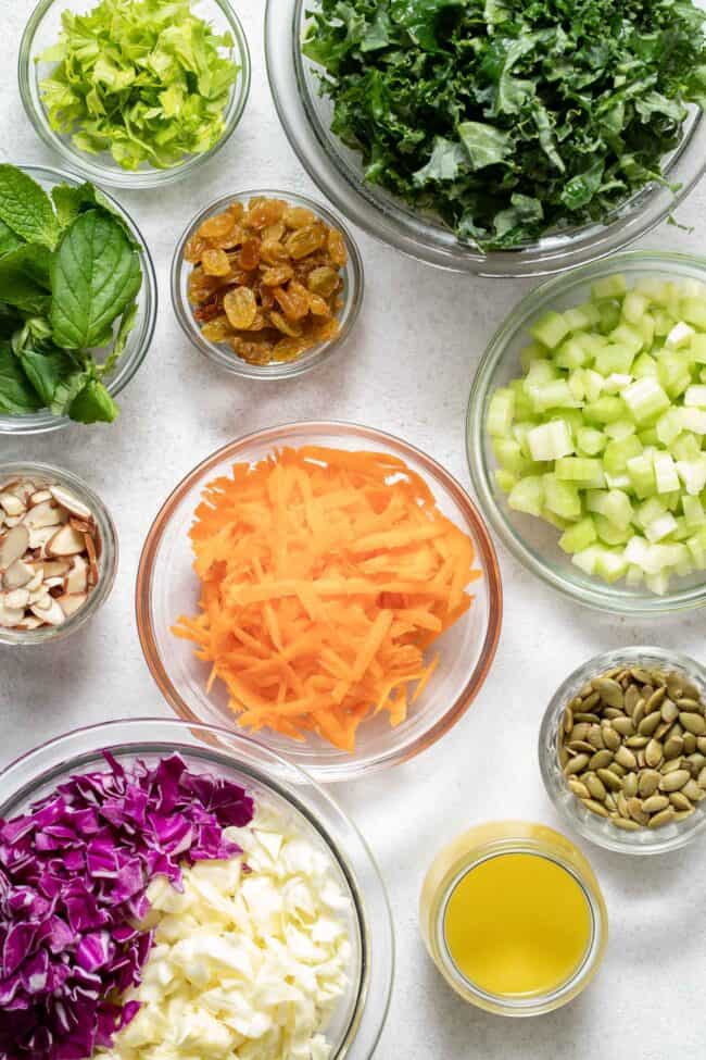 Clear glass mixing bowls filled with cabbage, carrots, celery and kale.
