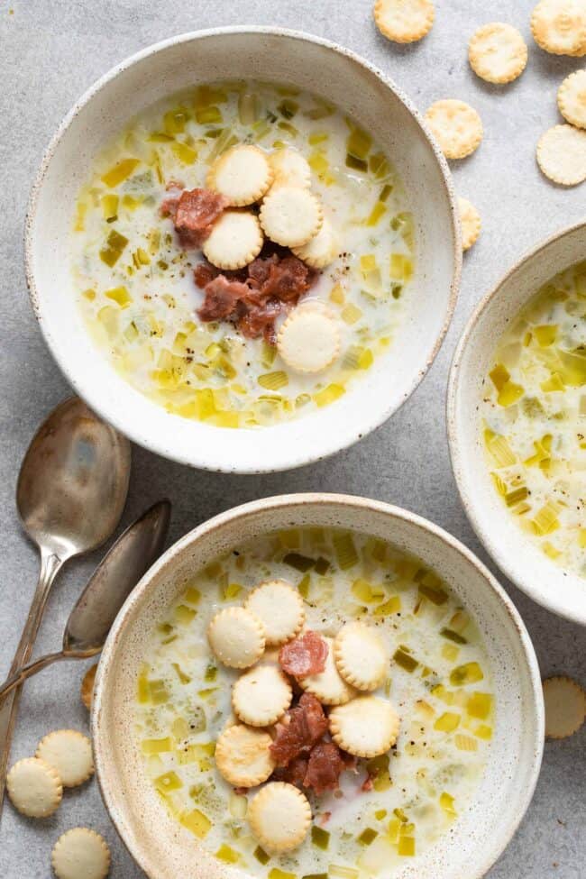 Two tan colored bowls filled with creamy clam chowder garnished with pieces of bacon and Oyster crackers.