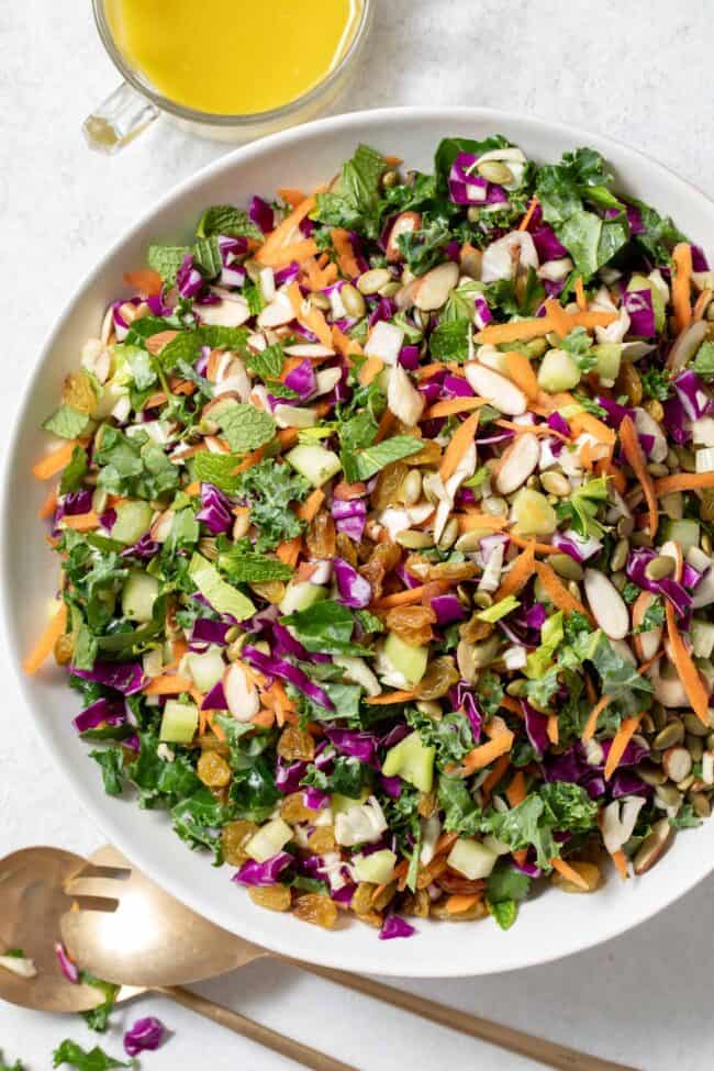 A white bowl filled with cut vegetables. A clear glass filled with dressing sits next to the bowl.