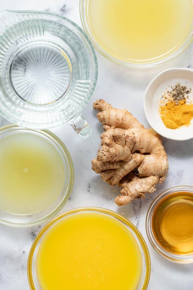 Small clear glass mixing bowls are filled with water citrus and honey sit next to fresh ginger root.