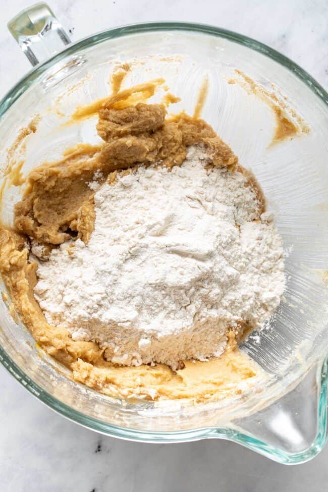 A glass mixing bowl filled with dough and flour.