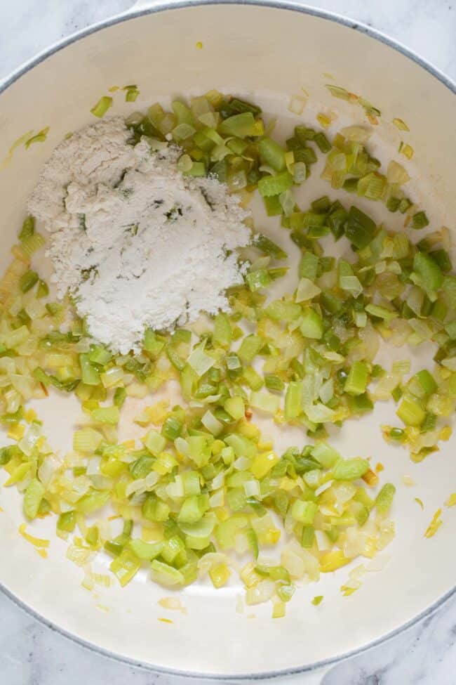 A large white pot filled with chopped sauteed vegetables and a scoop of white flour.