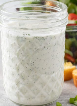 A clear glass mason jar filled with Vegan Ranch Dressing.