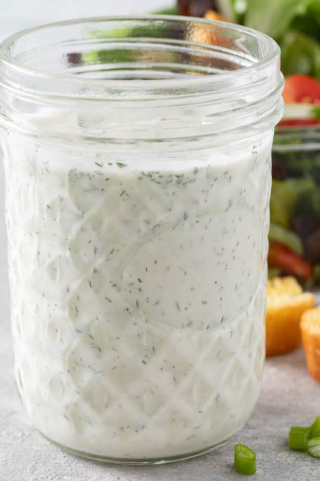 A clear glass mason jar filled with Vegan Ranch Dressing.