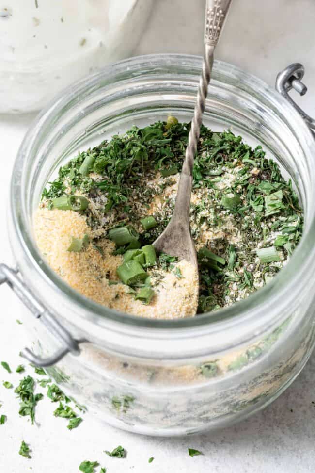 A mason jar filled with a mix of Homemade Ranch Seasoning. A small spoon rests in the jar.