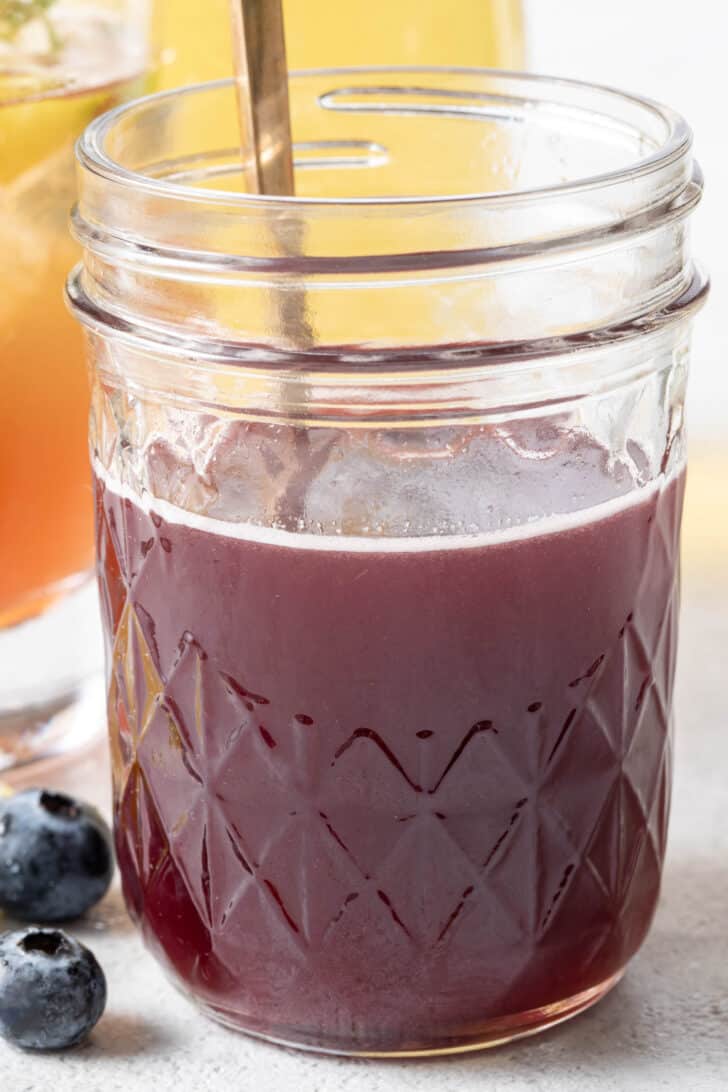 A clear mason jar filled with blueberry honey syrup.
