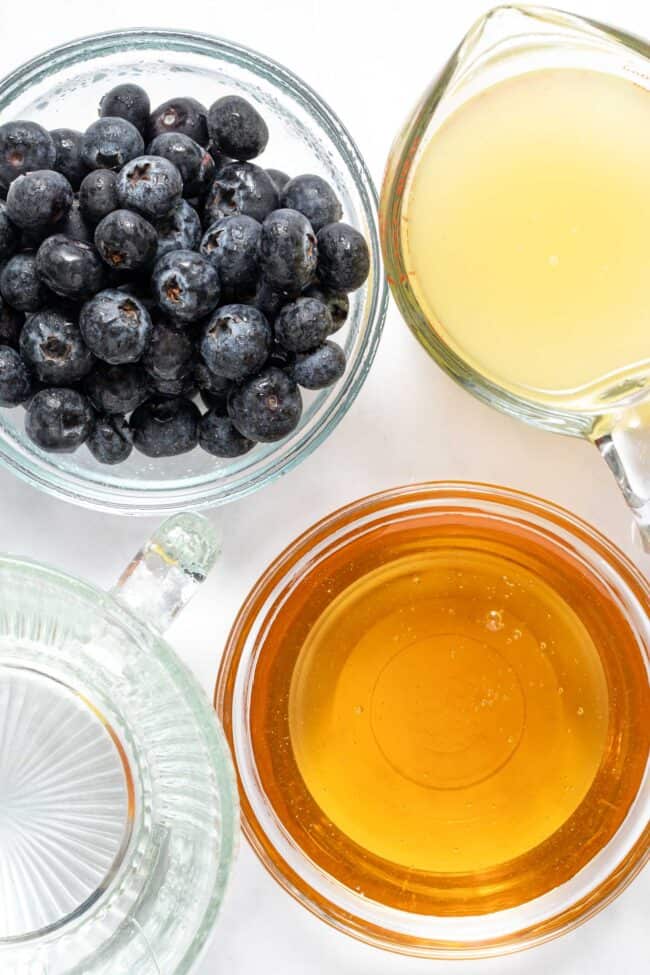 Four glass measuring cups filled with fruit, juice, honey and water..