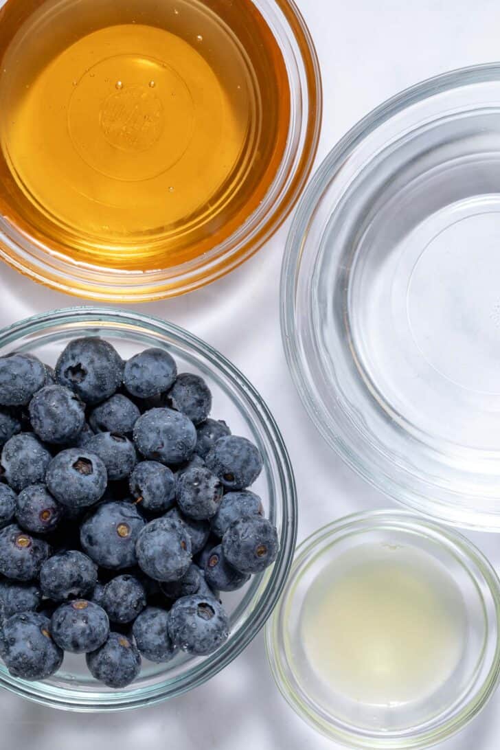 Four clear glass bowls filled with fruit, lemon juice, water and honey.