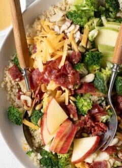 A white bowl filled with Broccoli Cheddar Quinoa salad. Salad spoons rest in the bowl.