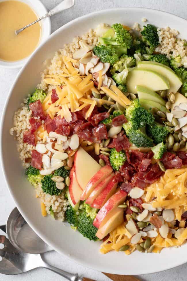 A white bowl filled with quinoa, chopped fruit, vegetables and nuts.