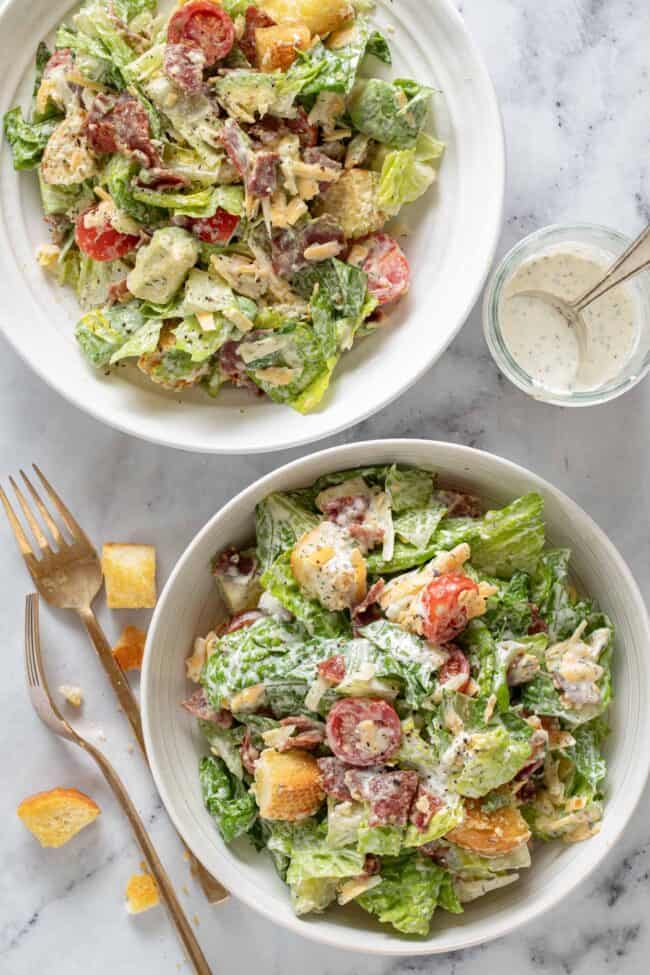 Two white bowls filled with salad tossed with homemade buttermilk ranch dressing.