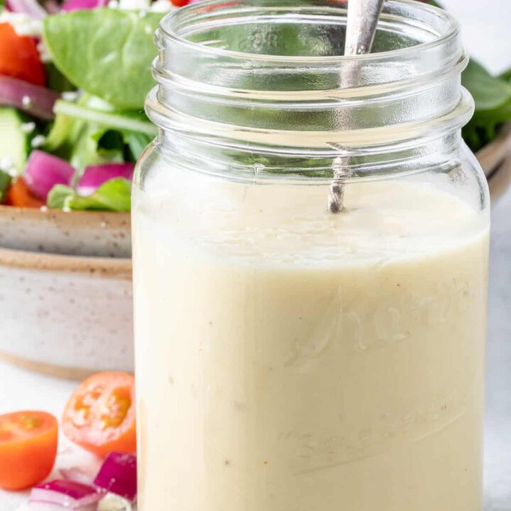 A clear mason jar filled with champagne vinaigrette. A tan colored bowl filled with salad sits behind the jar.