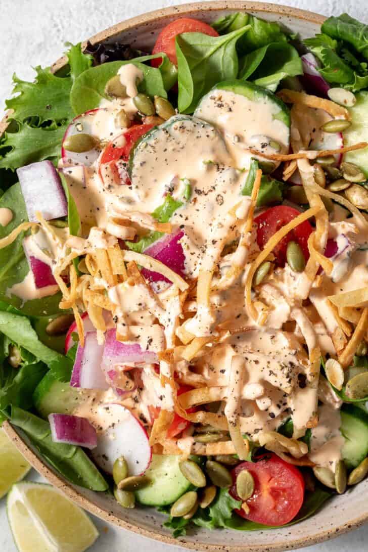 A tan colored bowl filled with mixed greens with cucumber, tomatoes, onion and radishes.