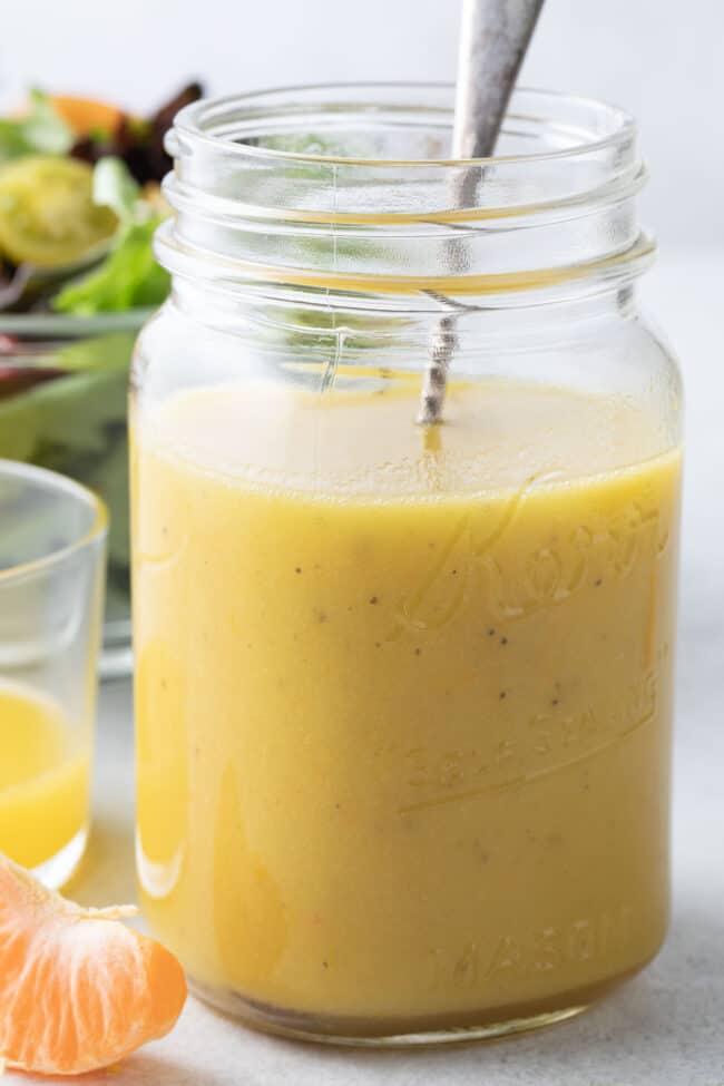 A clear glass mason jar filled with orange salad dressing.