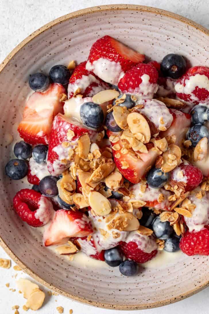 A tan colored bowl filled with mixed berries, toasted nuts and granola.