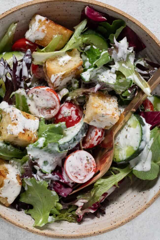 A tan bowl filled with salad tossed in dressing.