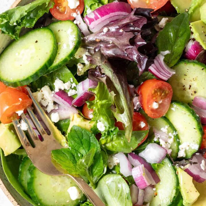 A tan colored bowl filled with Spring Mix Salad. A gold fork rests in the bowl.