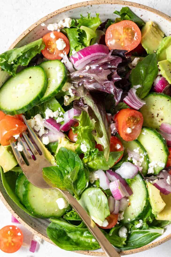 A tan colored bowl filled with Spring Mix Salad. A gold fork rests in the bowl.