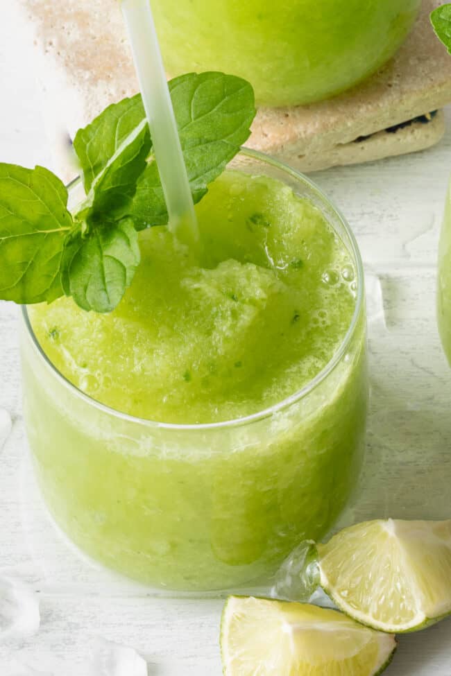 Two clear glasses filled with green frozen treat garnish with mint leaves.