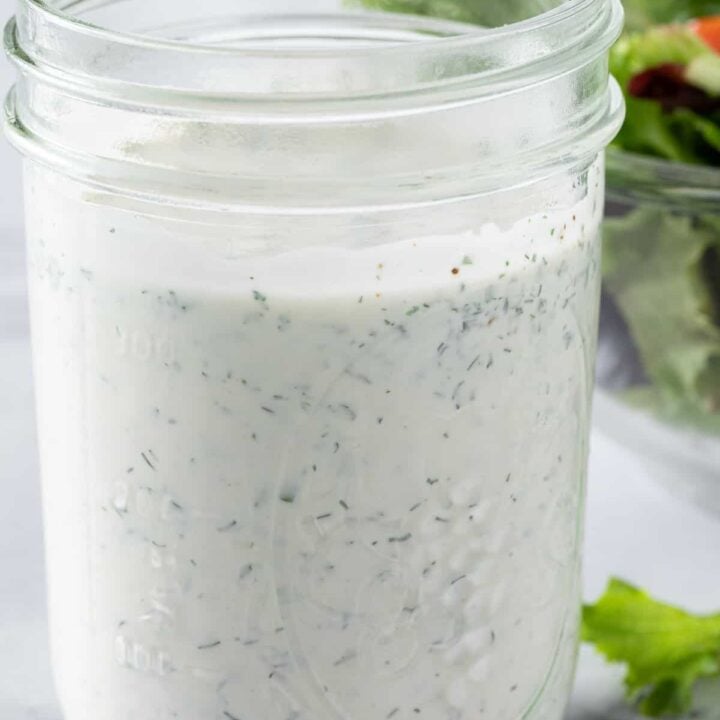 A mason jar filled with ranch dressing. A clear glass bowl filled with salad sits next to the jar.
