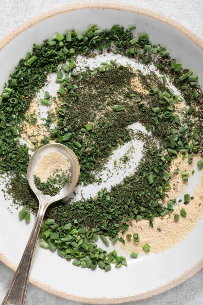 A white plate with dried spices scattered on it. A silver spoon rests on the plate.