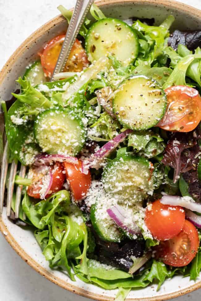A tan colored bowl filled with salad, cucumbers and cherry tomatoes tossed with dressing.