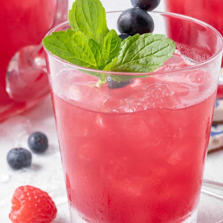 Two clear glasses and a glass pitcher are filled with Iced Blueberry Tea.